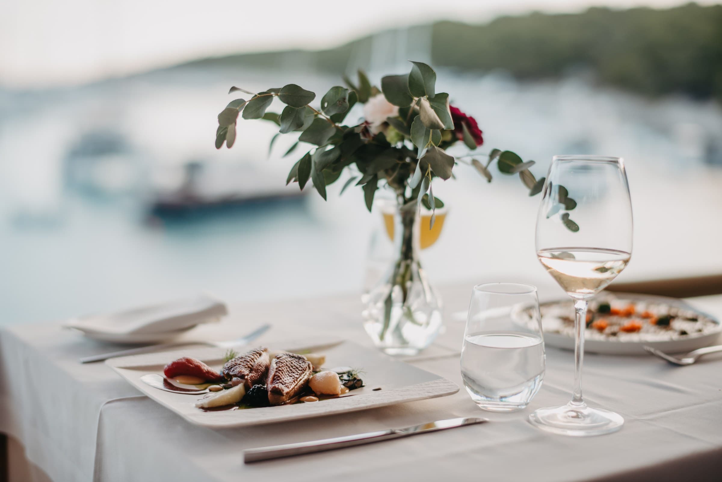 La pesca del día emplatada al borde de la mesa, detrás los barcos de la bahía de Vinogradišće, Zori Restaurant, Palmižana